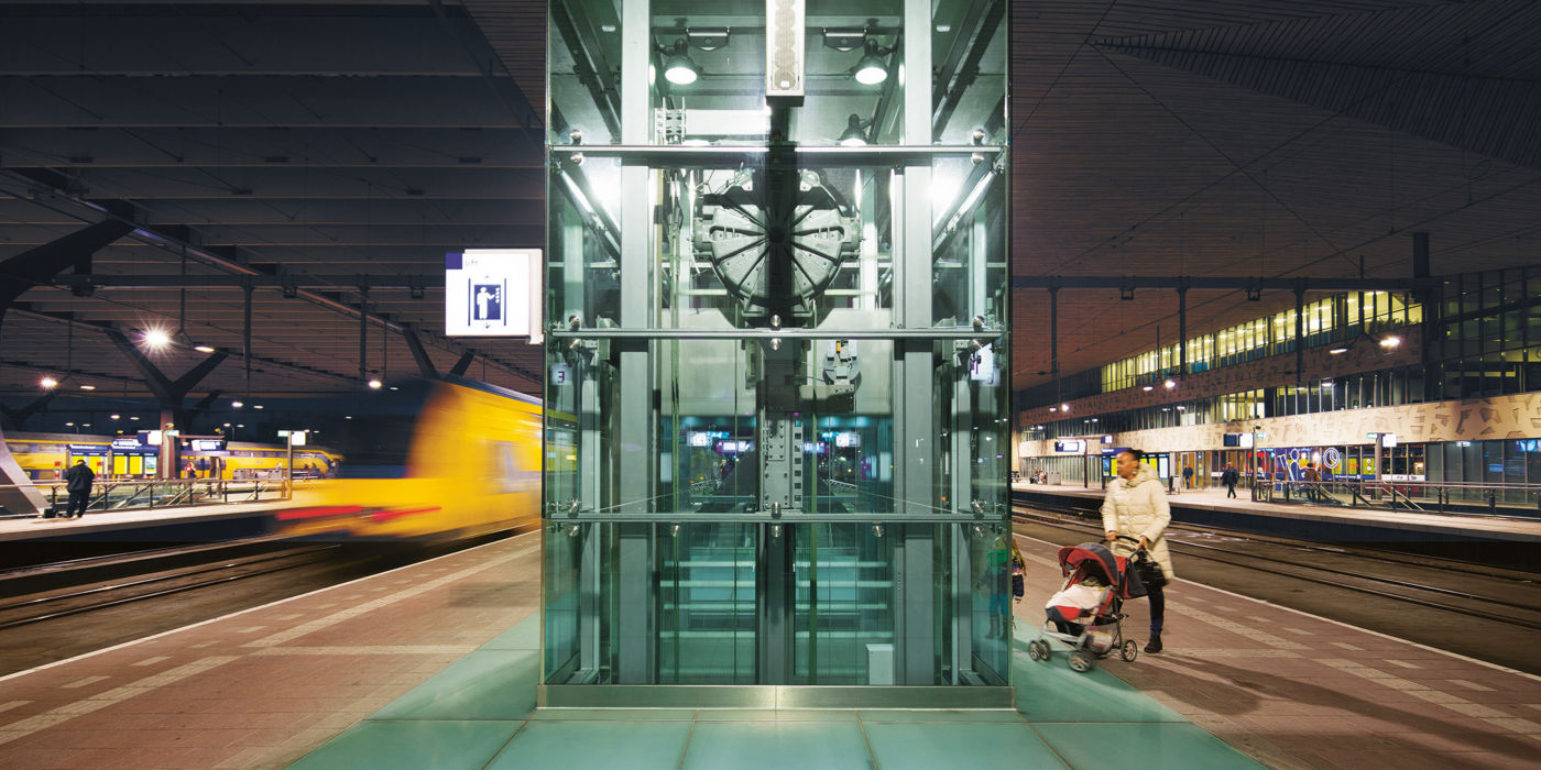 Person with a pram getting ready to enter an elevator on a nightly railway platform.